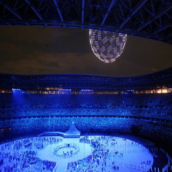 A scene from the 2020 Summer Olympics opening ceremony at the Olympic Stadium, with drones flying around and creating the official logo of the Games